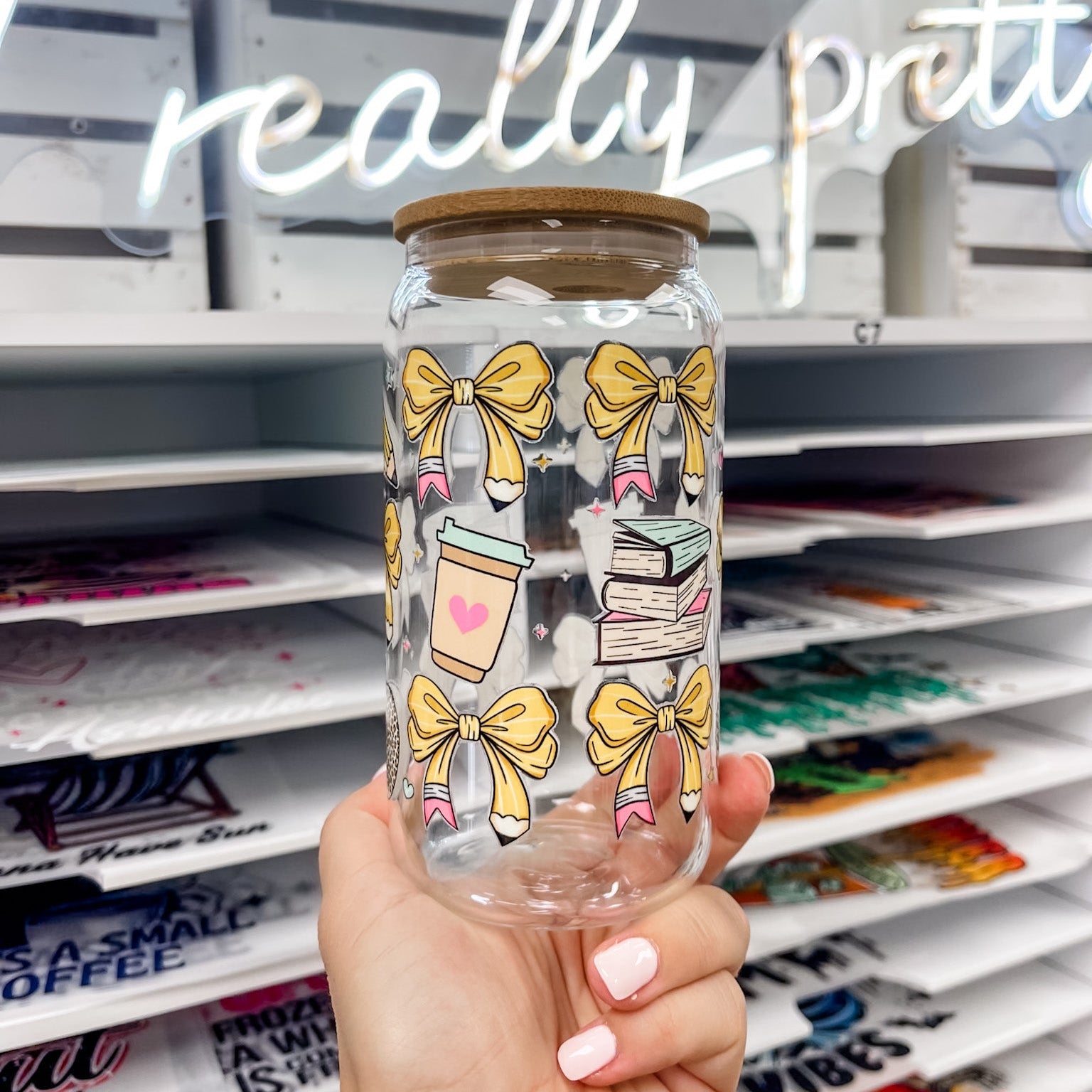 16 oz glass can featuring a teacher-themed UV DTF transfer with yellow pencil bows, coffee cup, and books, showcasing a durable waterproof custom UV sticker wrap