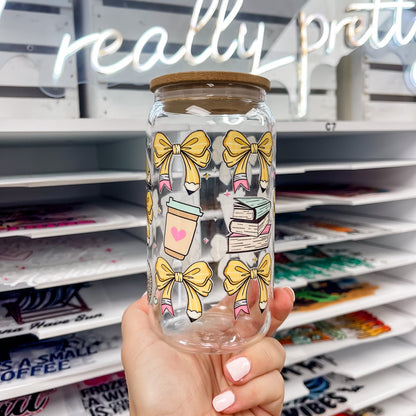 16 oz glass can featuring a teacher-themed UV DTF transfer with yellow pencil bows, coffee cup, and books, showcasing a durable waterproof custom UV sticker wrap